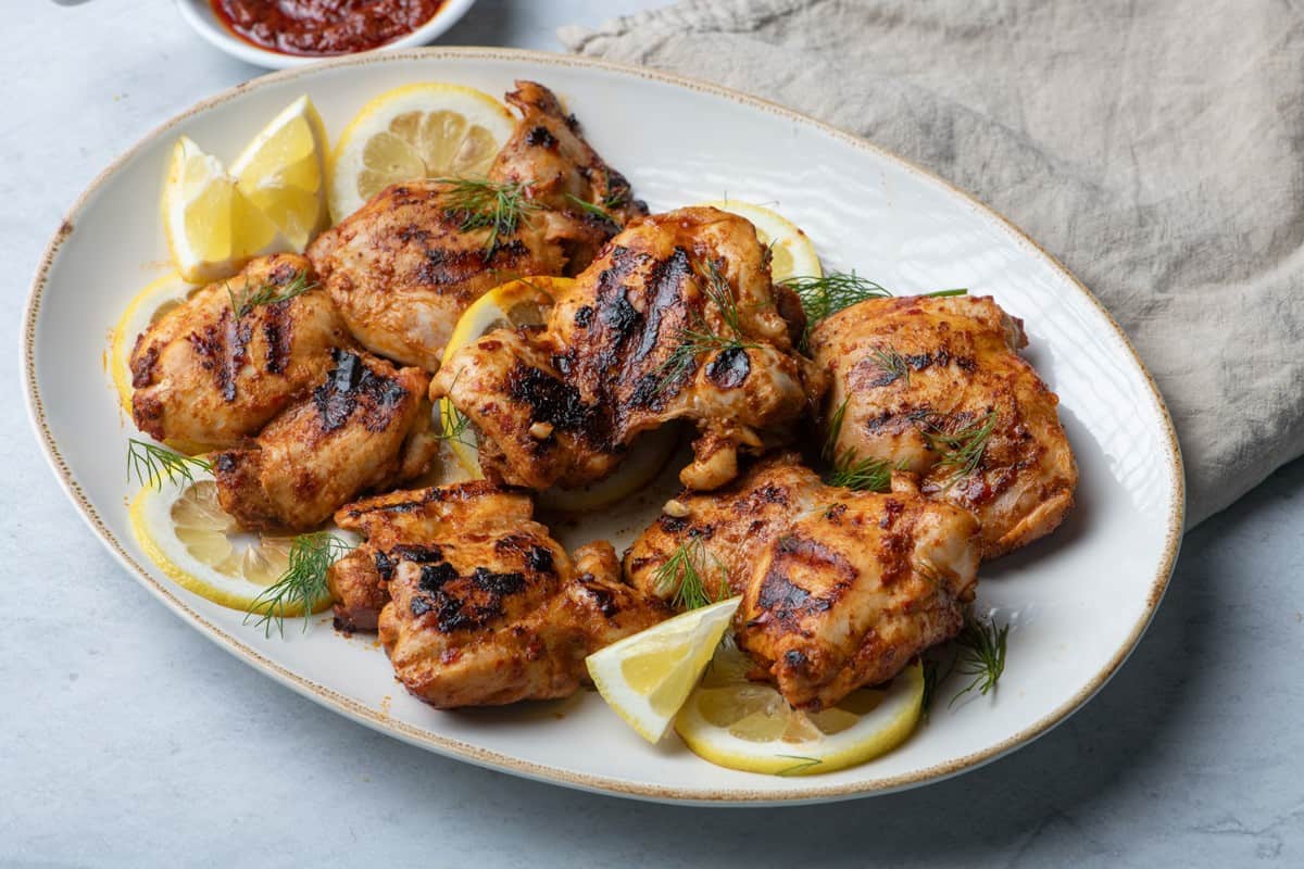 Grilled harissa chicken on serving dish with lemon slices.