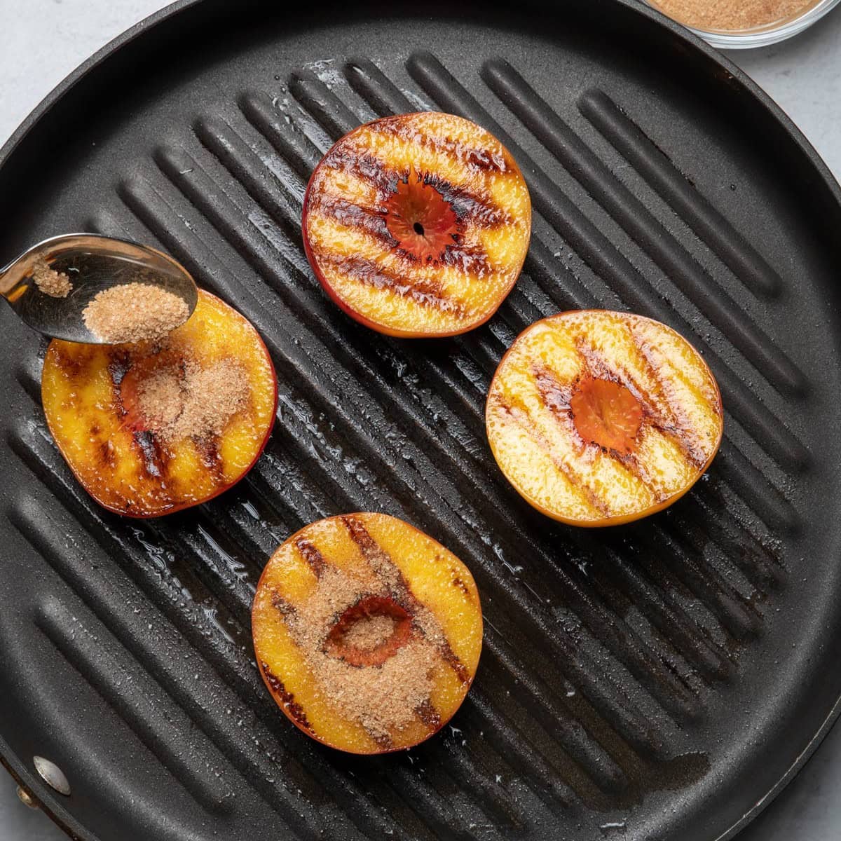 Spoon sprinkling brown sugar and cinnamon sugar over peaches on grill pan after itโs cooked.