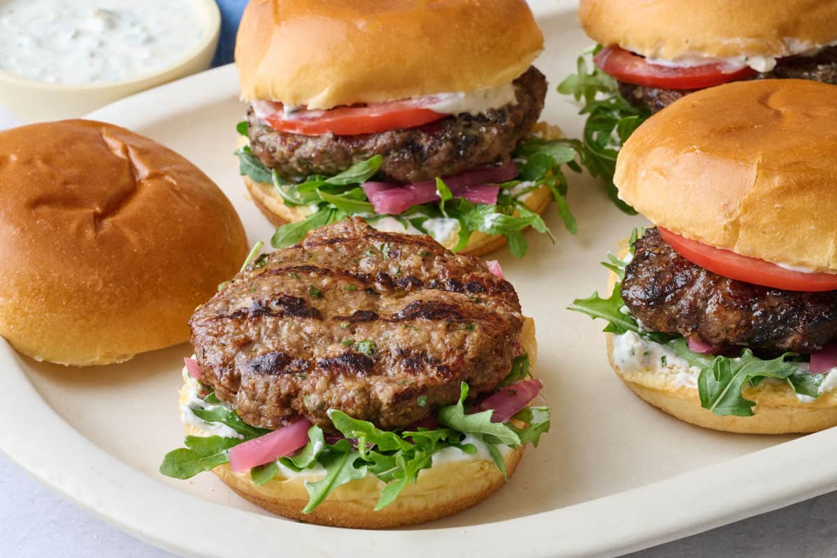 Assembled burgers on a platter topped with yogurt, lid off one burger, and yogurt dish nearby.