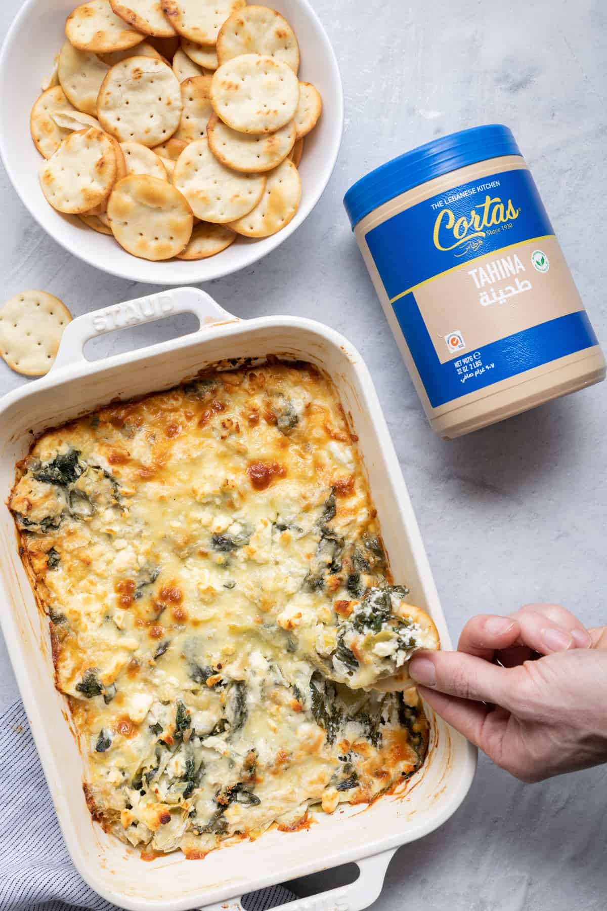 Artichoke tahini dip with pita cracker dipping into dip
