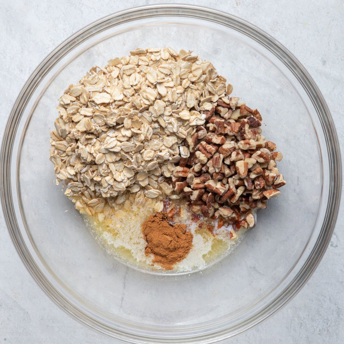 Bowl with melted butter, maple syrup, oats, pecans and cinnamon before mixing.