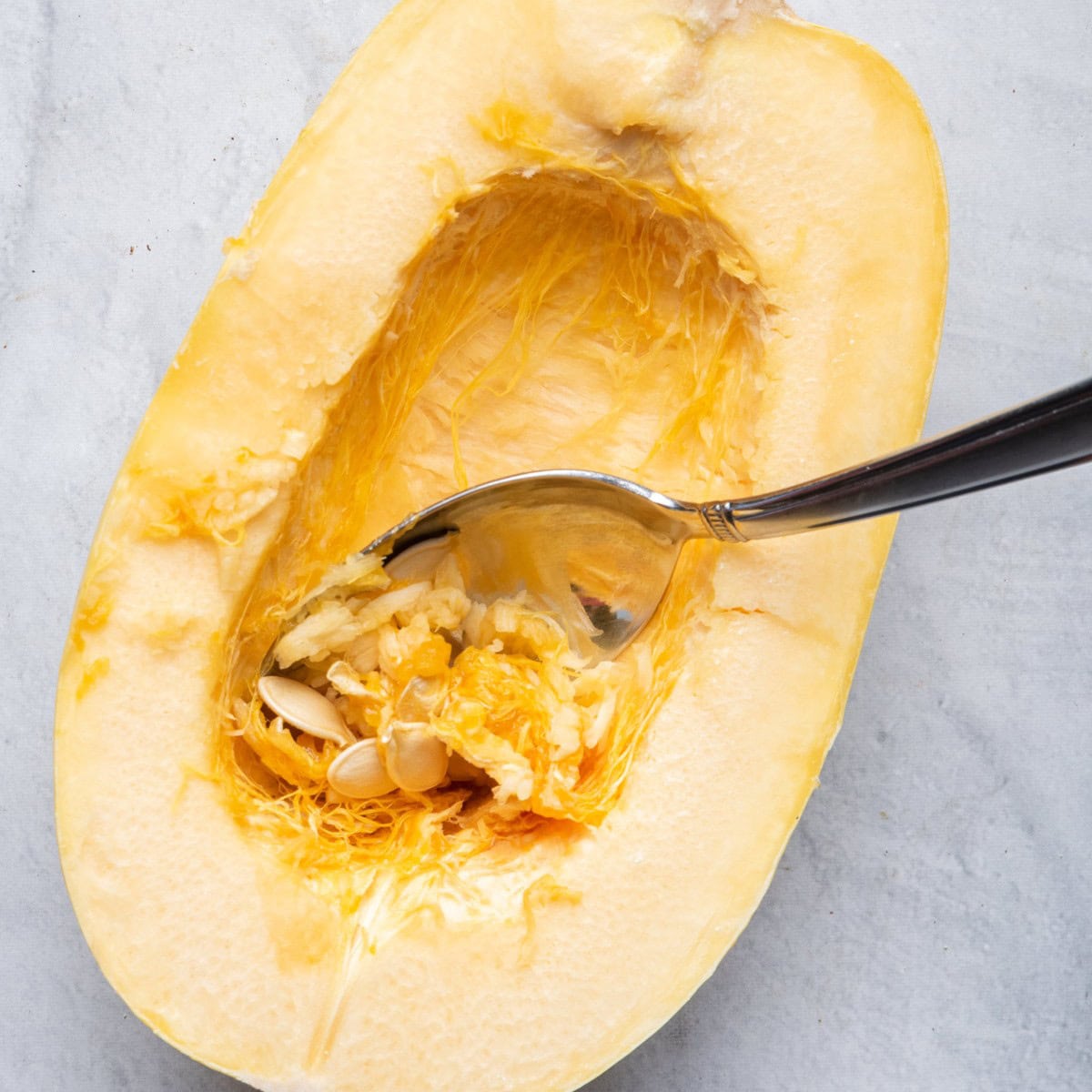Scooping out seeds from spaghetti squash with spoon.