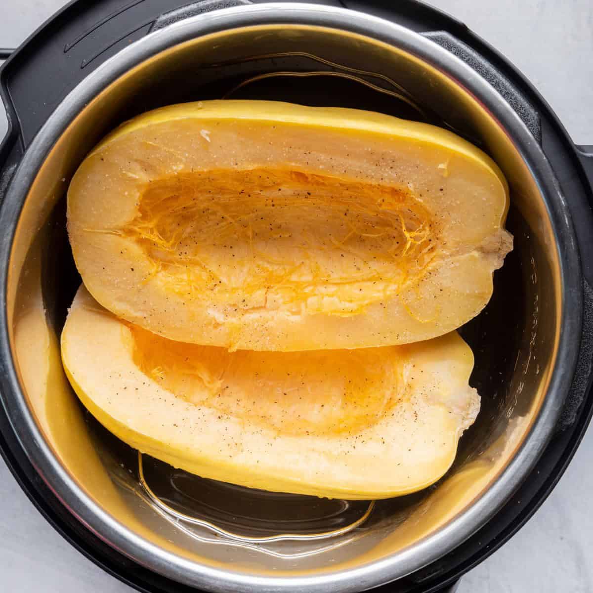 Two spaghetti squash halves inside instant pot with trivet with salt and pepper.