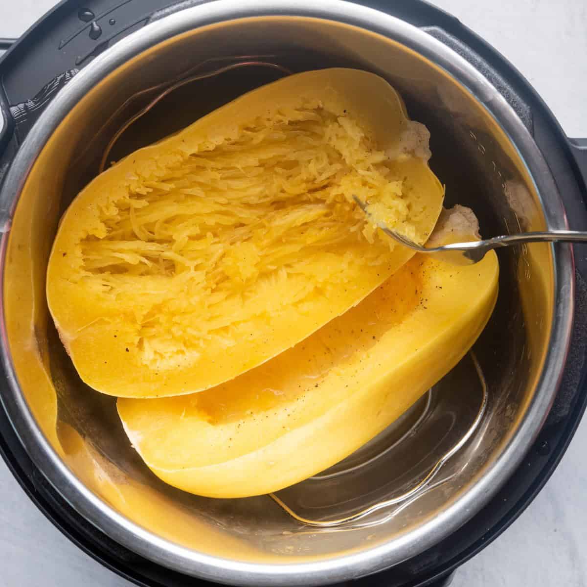Cooked spaghetti squash in pot with fork pulling strands.