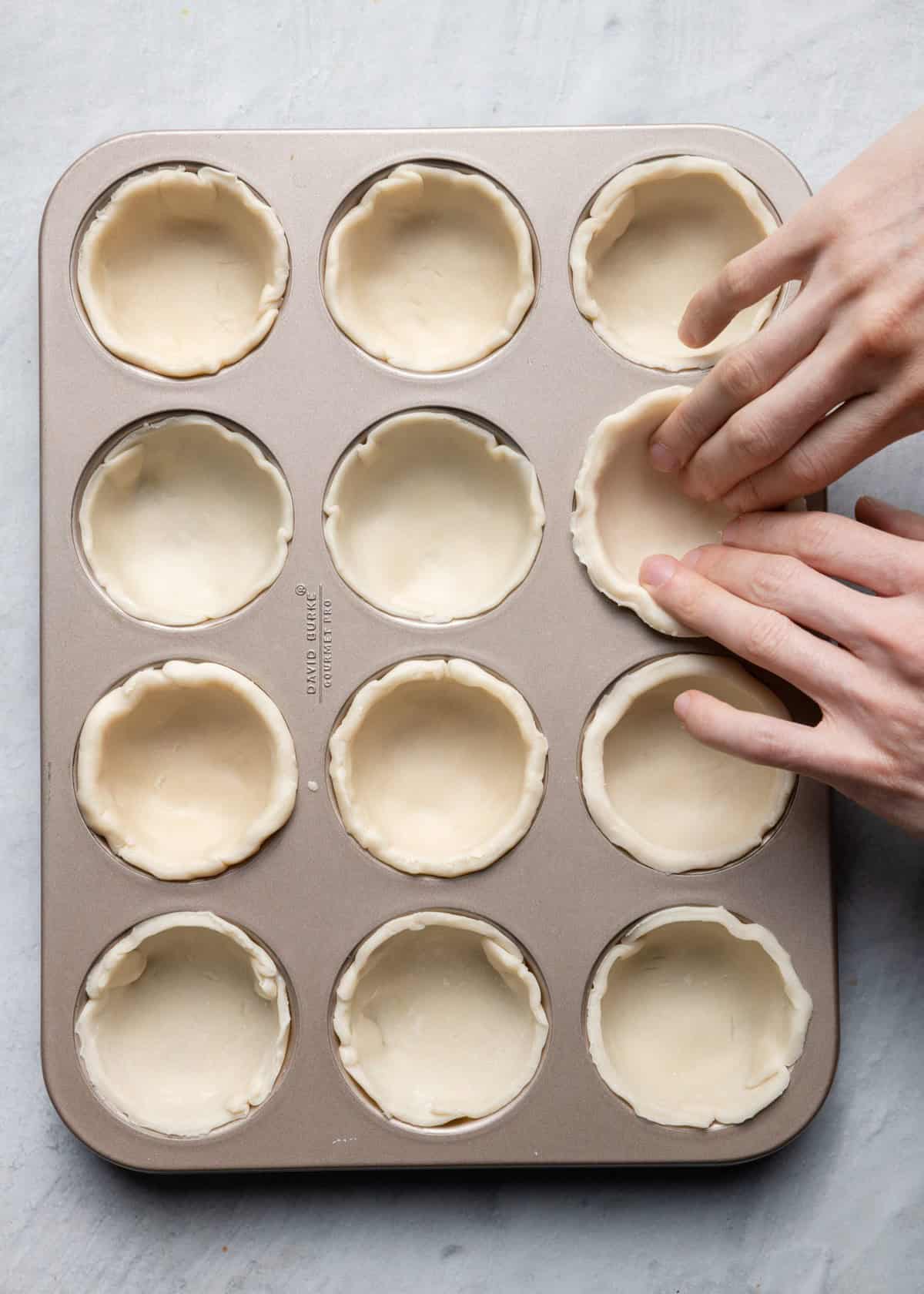 Some dough in half the muffin cups, finger pushing dough in the tin to form it.