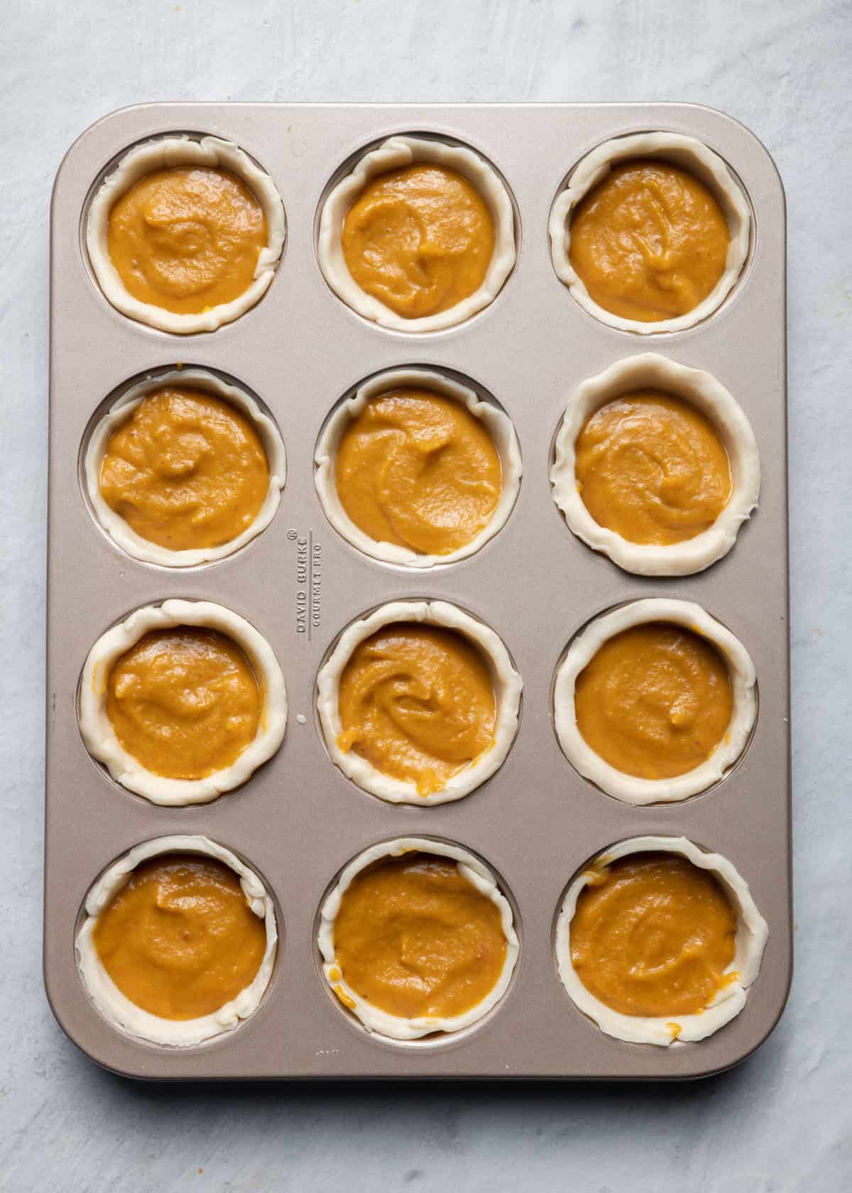 One muffin tin full of the crust and filling before baking.