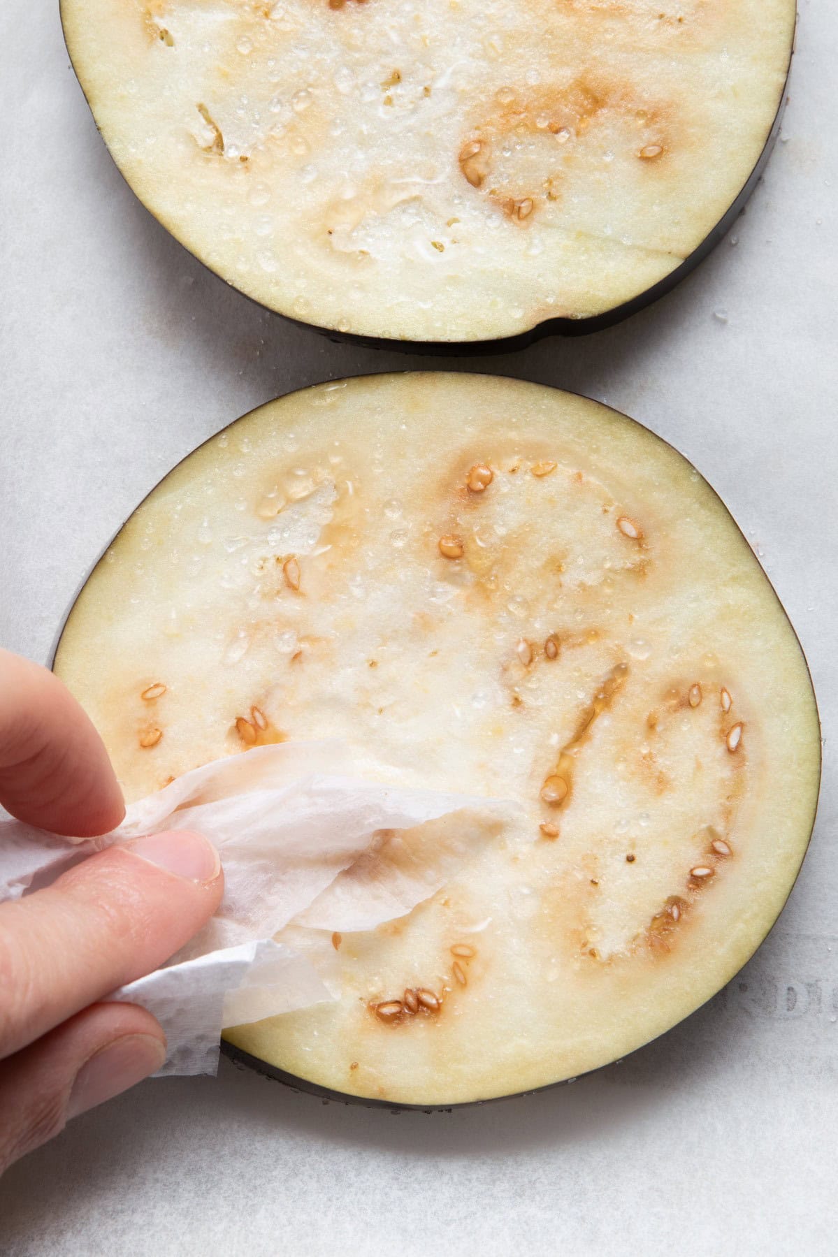 Eggplant slices showing beads of sweat and paper towel dabbing them dry.