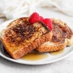 Three pieces of french toast on a plate topped with raspberries and syrup.