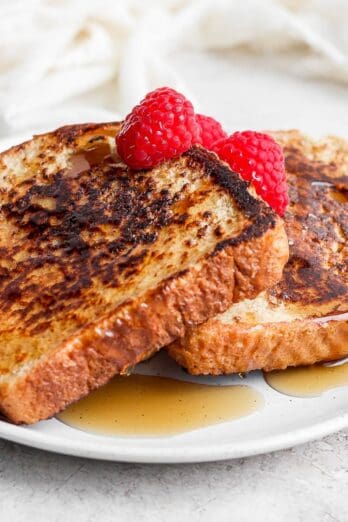 Three pieces of french toast on a plate topped with raspberries and syrup.