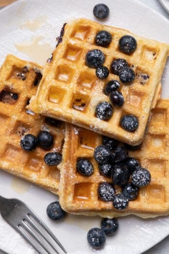 Plate of waffles with blueberries, powdered sugar and maple syrup on top.