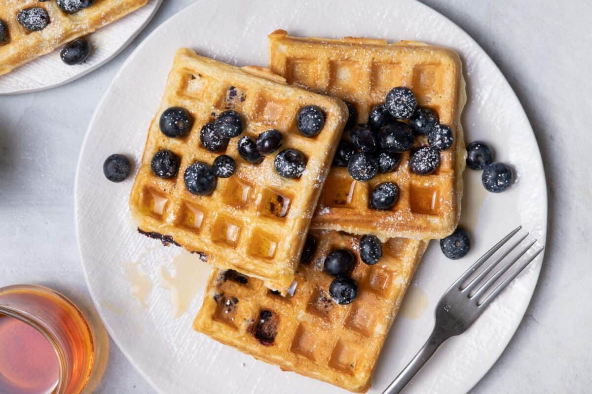 Plate of waffles with blueberries, powdered sugar and maple syrup on top.