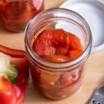 Roasted peppers in a jar with no lid, with another jar of roasted peppers and cut peppers nearby.
