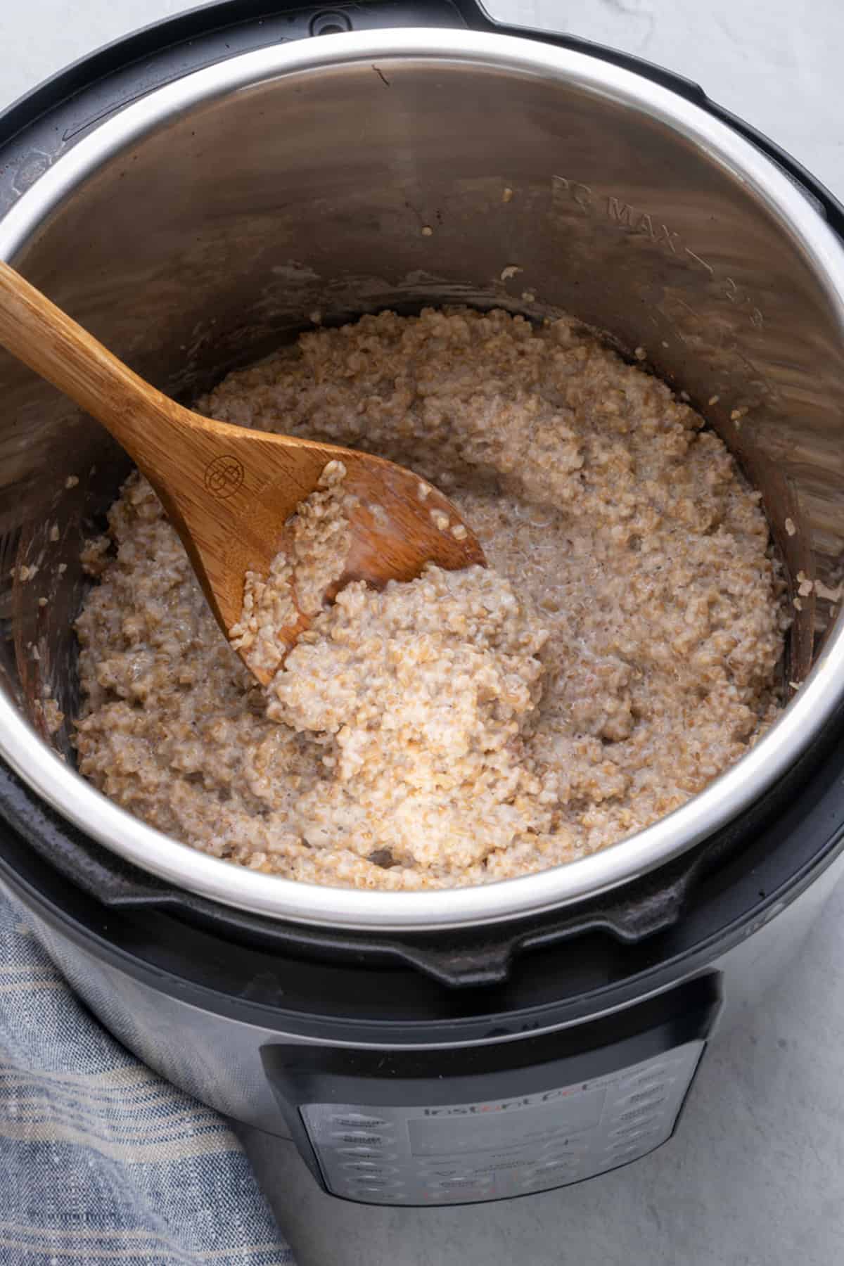 Steel cut oatmeal cooked inside instant pot with wooden spoon inside stirring