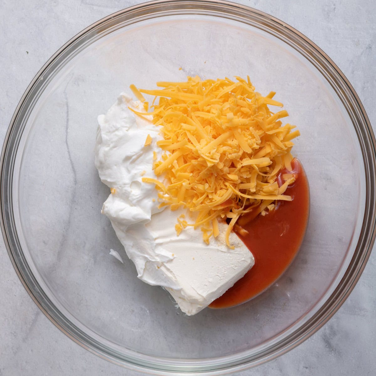 Bowl with cream cheese, greek yogurt, buffalo sauce, garlic powder, onion powder and cheese before mixed.