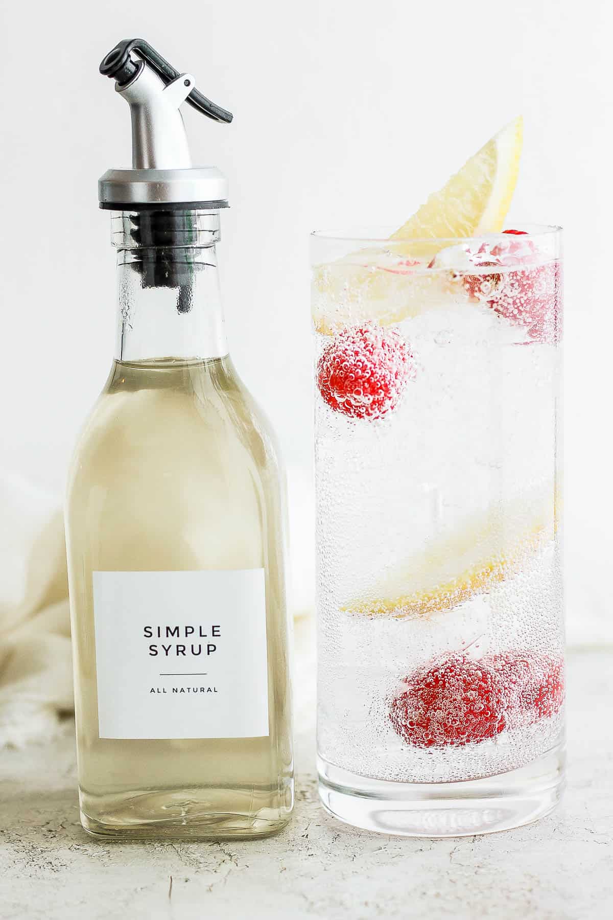 Bottle of simple syrup shot next to tall glass of carbonated water sweetened with simple syrup