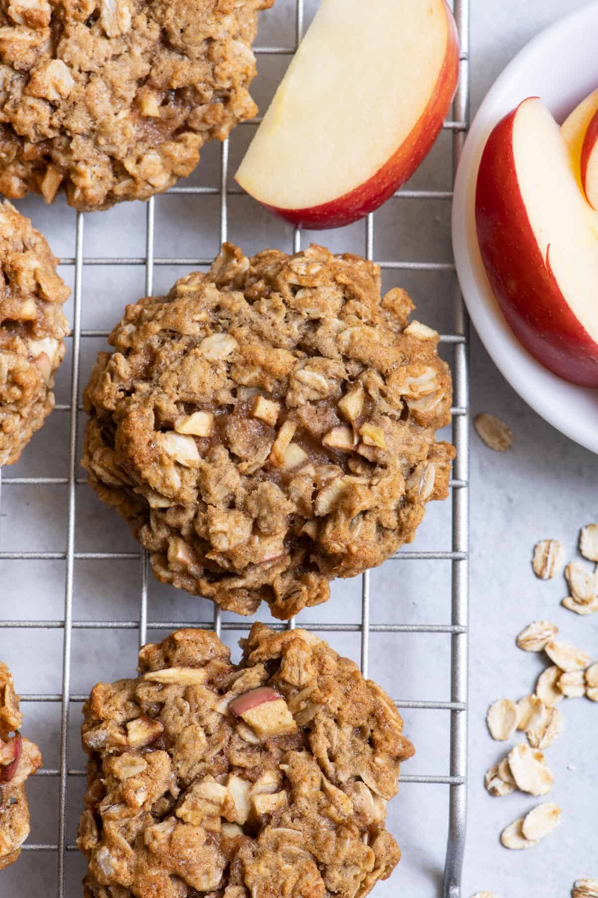 close up of cookie on wire cooling rack with slices of apples in white bowl