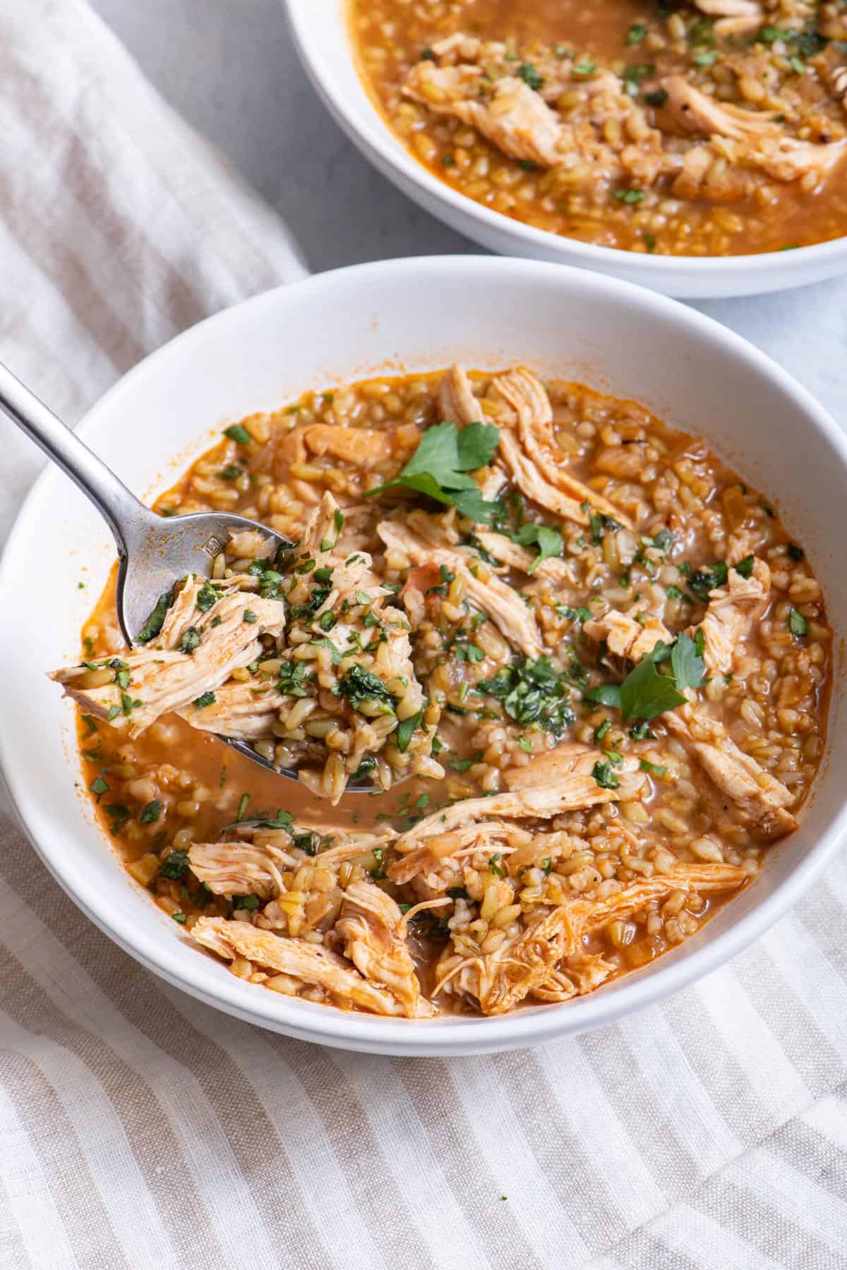 bowl of soup with spoon dipping out a serving with another bowl of recipe in background