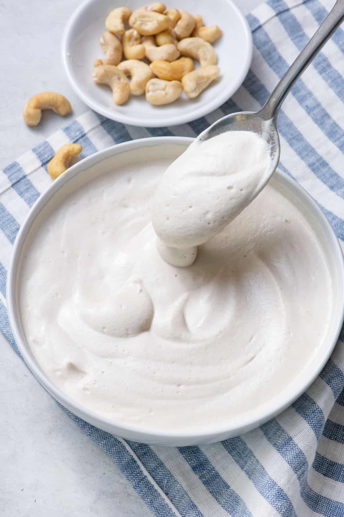 action of spoon dipping into a bowl of cashew cream with a small dish of cashews