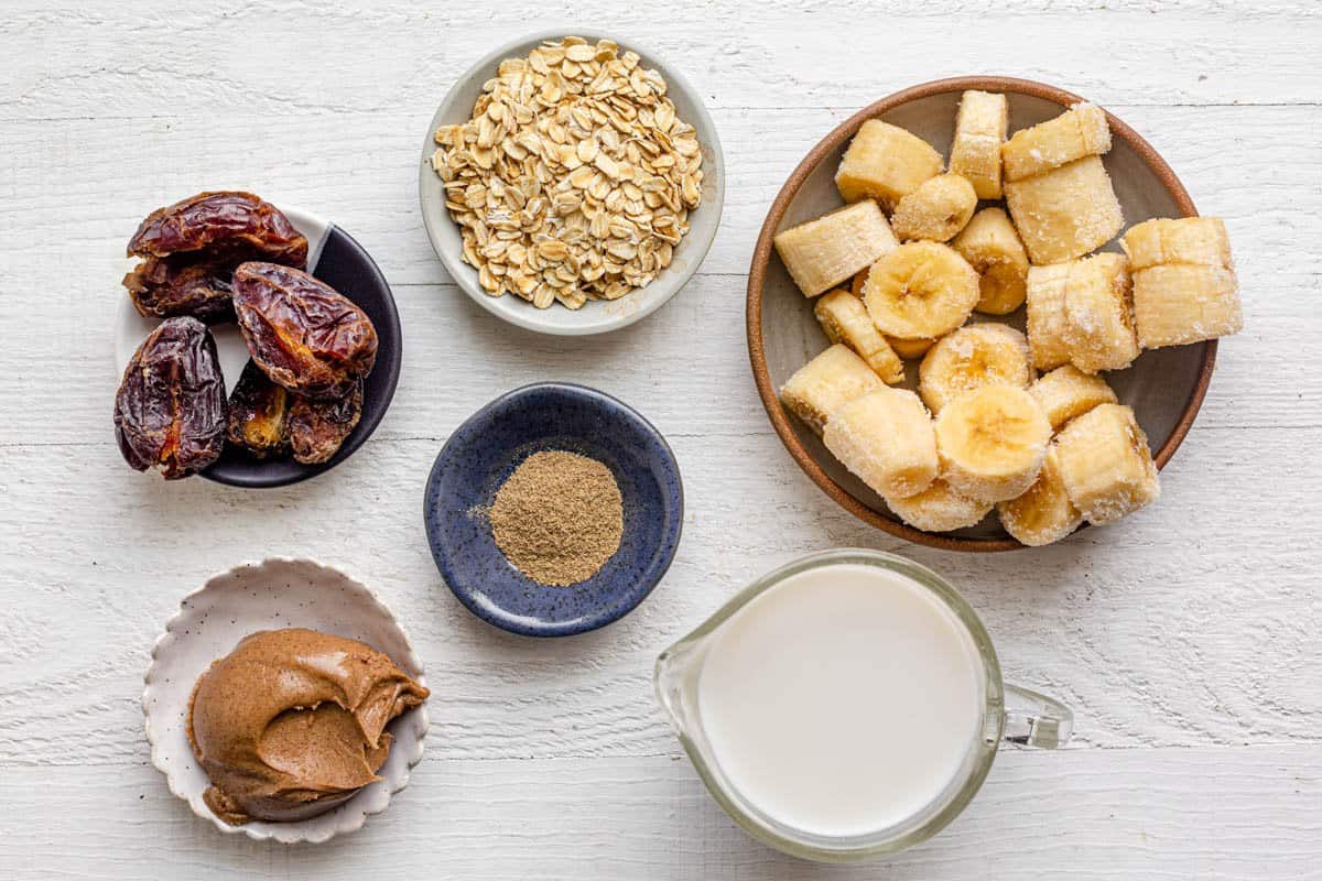 Ingredients for recipe in individual bowls: Dates, rolled oats, cardamom, almond butter, almond milk, and frozen banana chunks.