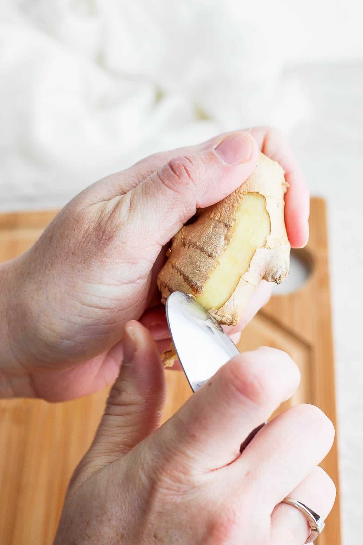 Close up showing how to use a spoon to peel fresh ginger.