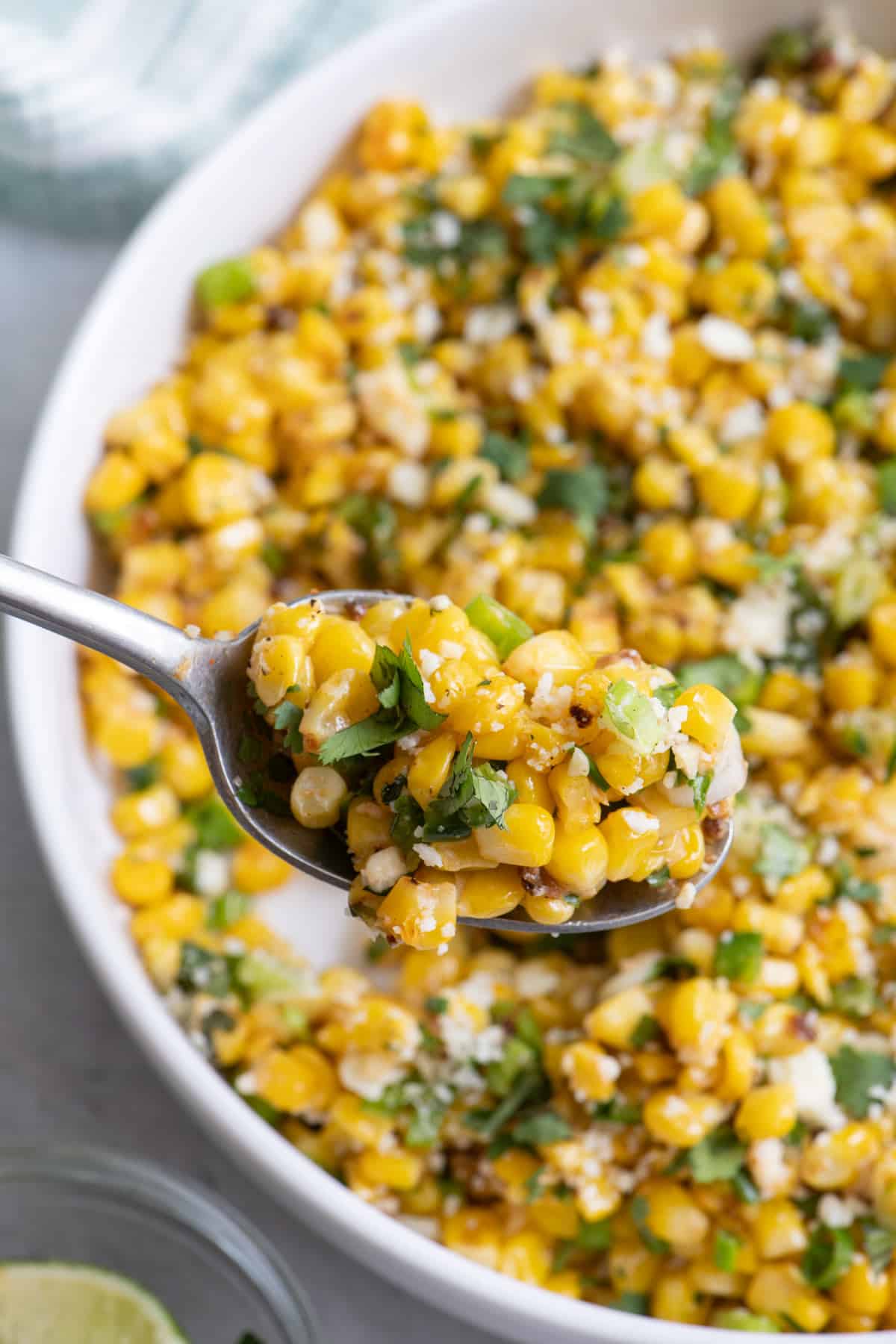 Close up of spoon scooping some Mexican street corn salad from large serving dish.