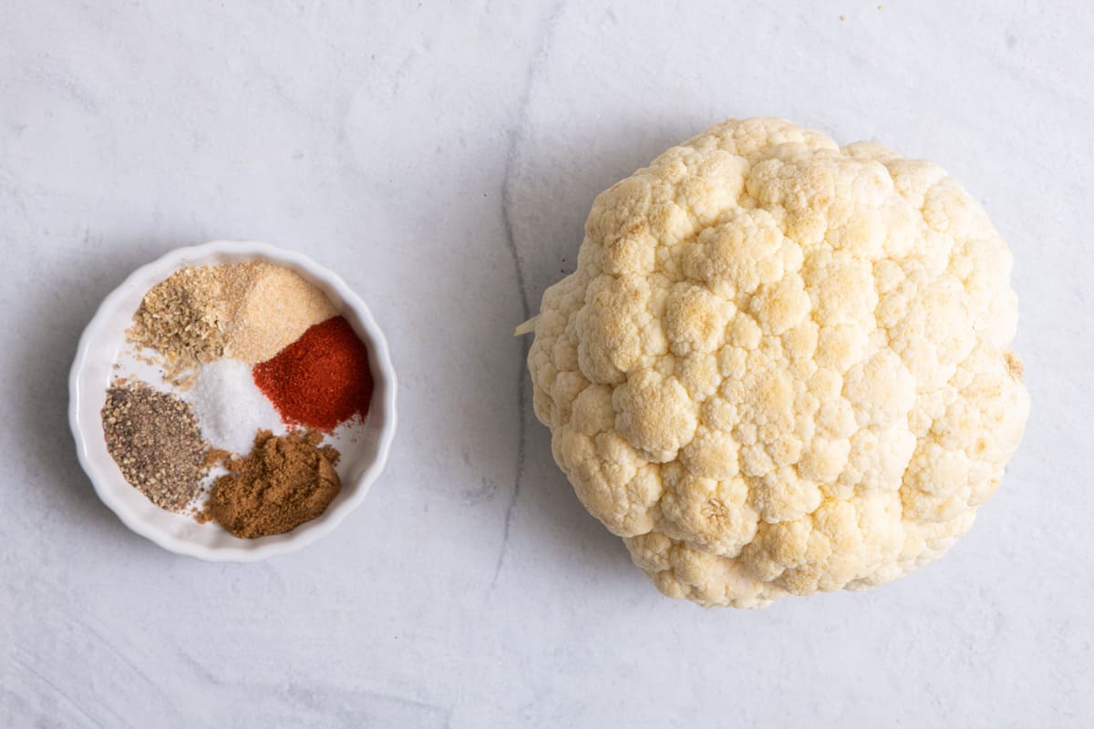 Ingredients to make the recipe: head of cauliflower and spices in bowl.