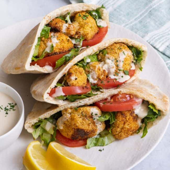 Three cauliflower pitas on a dish resting on top of one another with a small dish of tahini nearby.