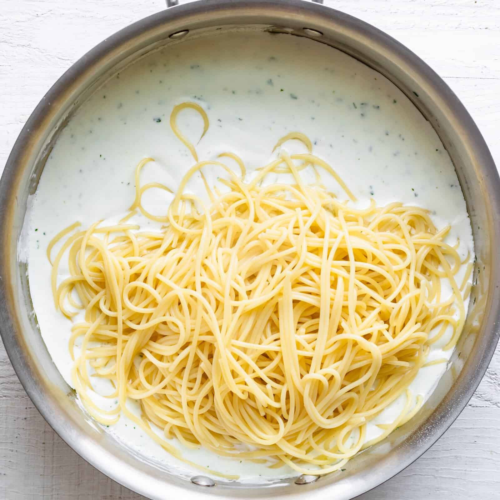 Spaghetti added to the pot of yogurt sauce.