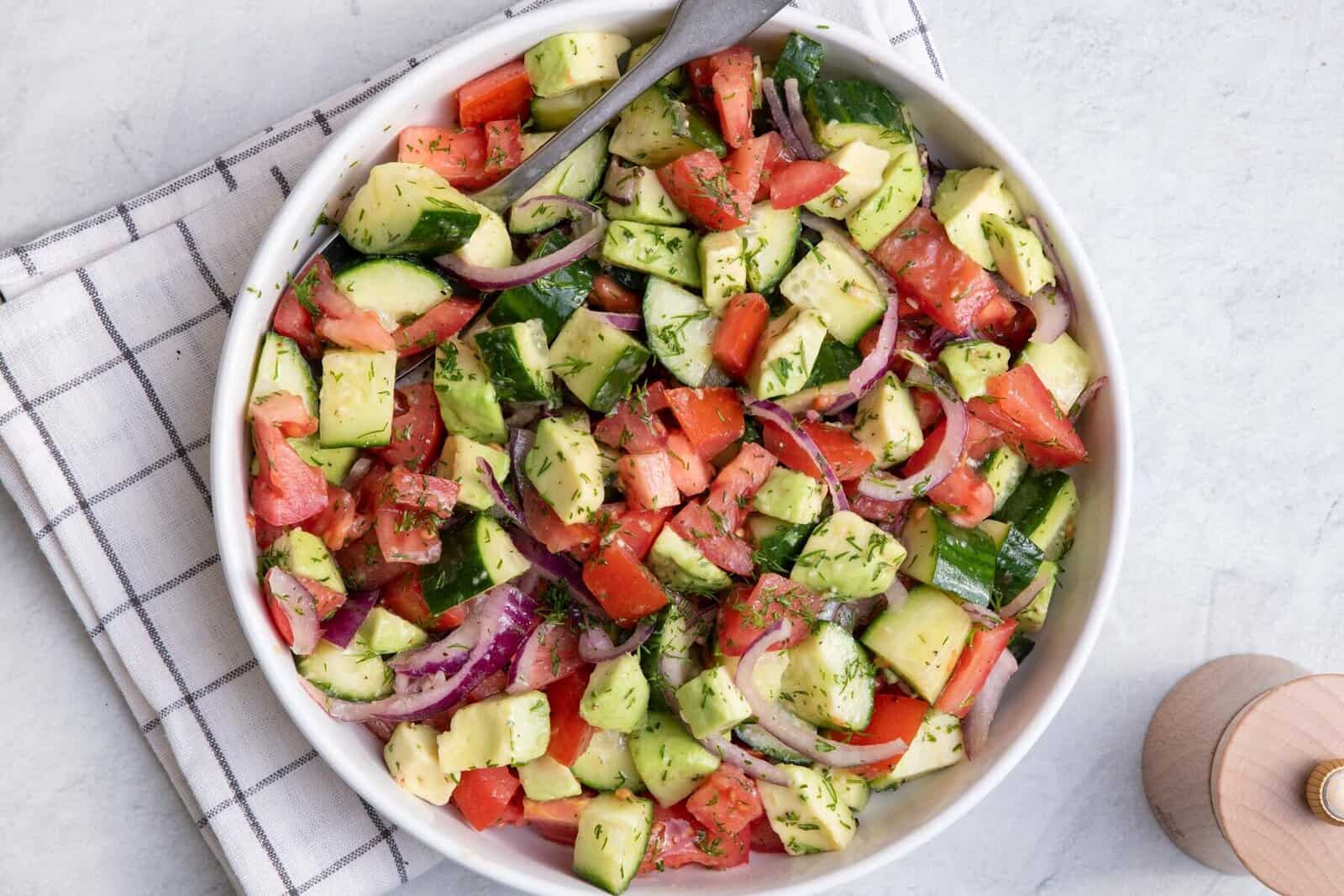 Cucumber Tomato Avocado Salad in a bowl with spoon resting in it. 