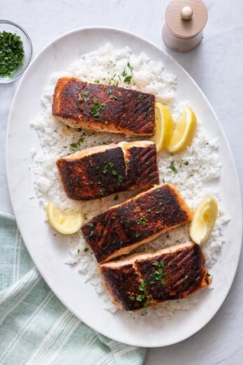 Overhead shot of 4 cooked salmons on a large oval white plate over rice and garnished with parsley and lemon wedges.
