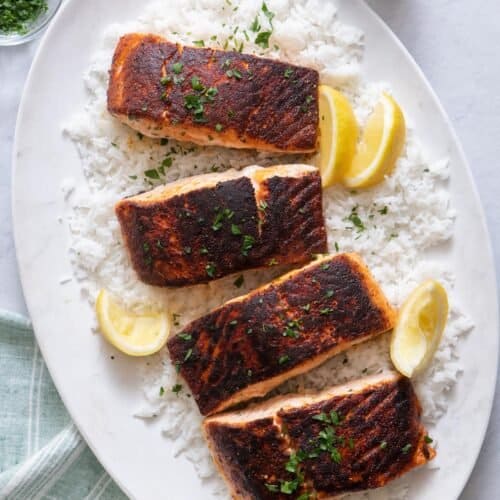 Overhead shot of 4 cooked salmons on a large oval white plate over rice and garnished with parsley and lemon wedges.