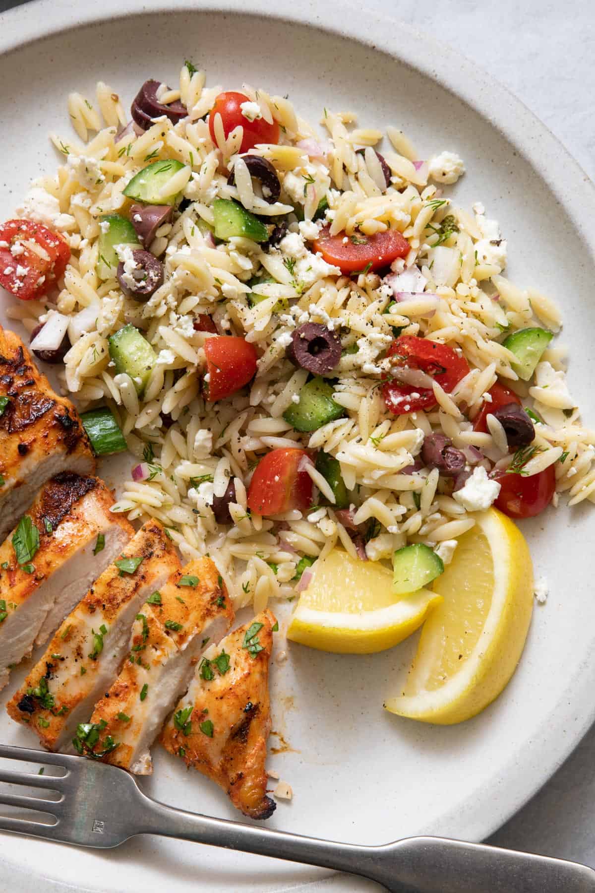 Orzo salad on plate next to sliced yogurt chicken with lemon wedges and a fork on plate.