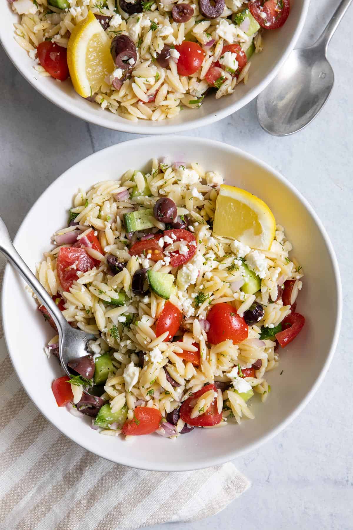 One of two bowls of Greek orzo salad with a spoon in dish.