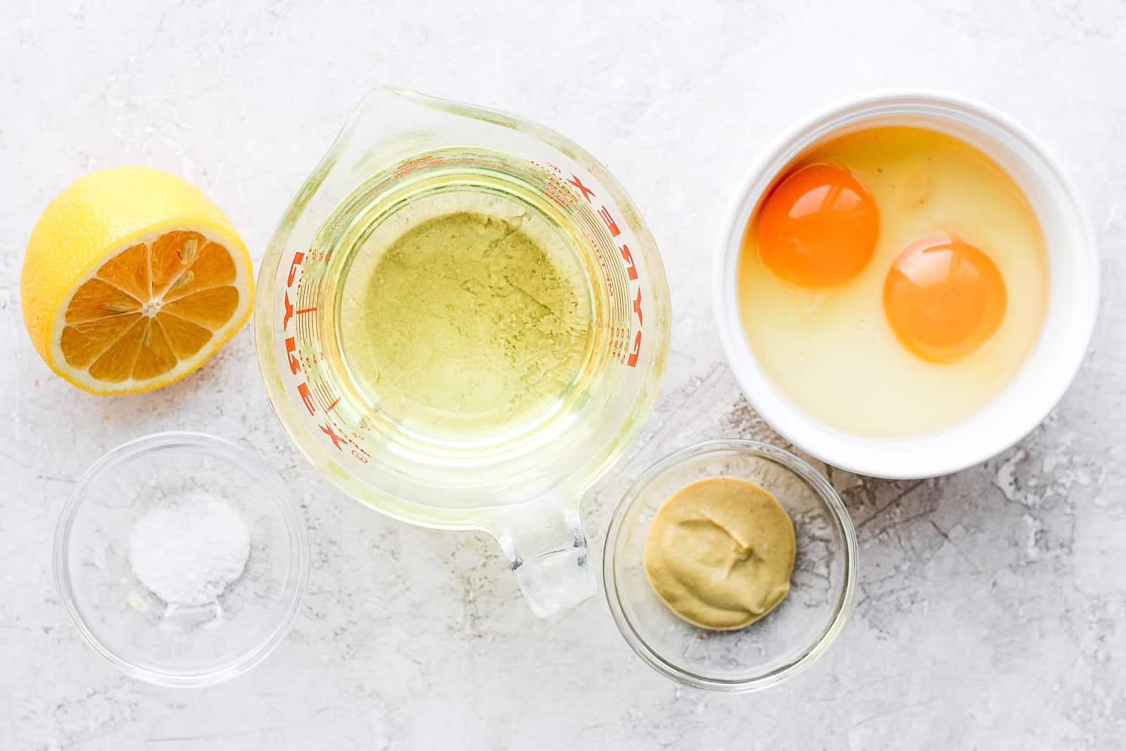 Ingredients for spread recipe: half cut lemon, salt, oil, 2 cracked eggs in bowl, and dijon mustard.