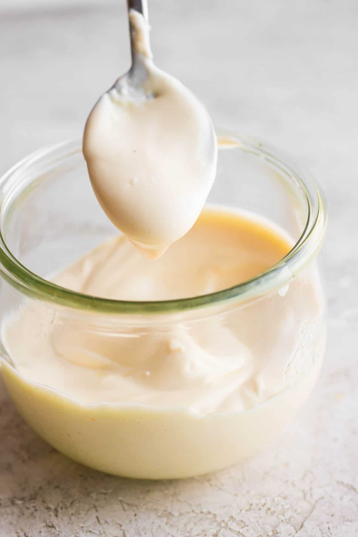 Spoon dipping out fresh made mayonnaise from glass jar.