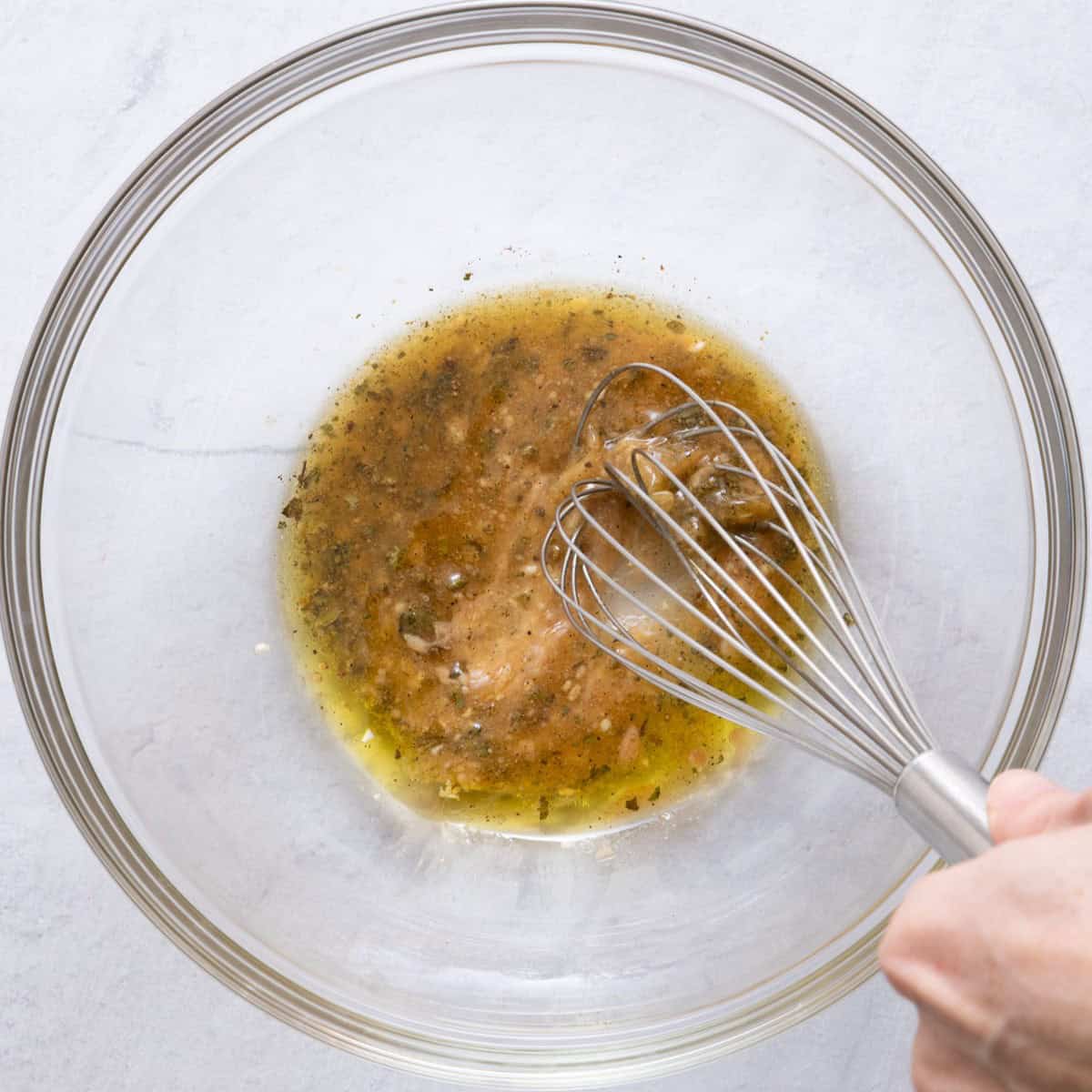 A large bowl filled with the dressing ingredients being whisked.