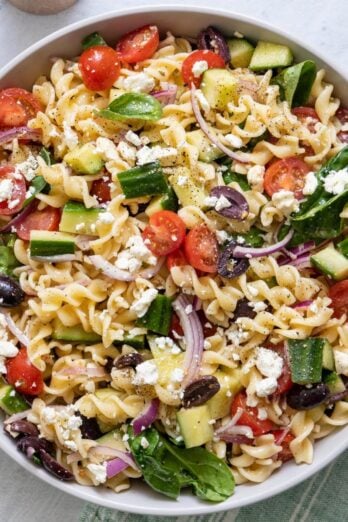 Mediterranean pasta salad in a serving bowl with a spoon resting inside.
