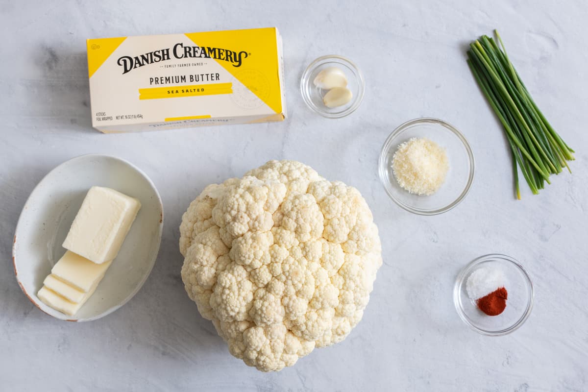 Ingredients for roasting recipe: butter, whole head cauliflower, garlic, spices, and fresh chives.