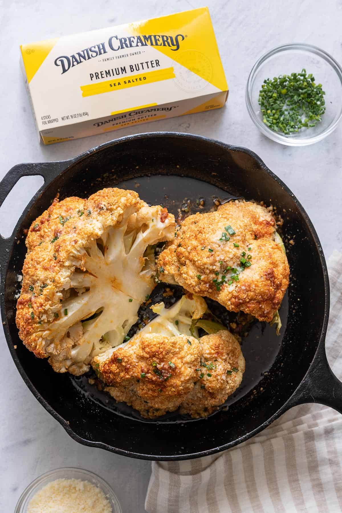 Whole roasted cauliflower with a box of Danish Creamery Premium butter sticks, fresh chives to garnish.