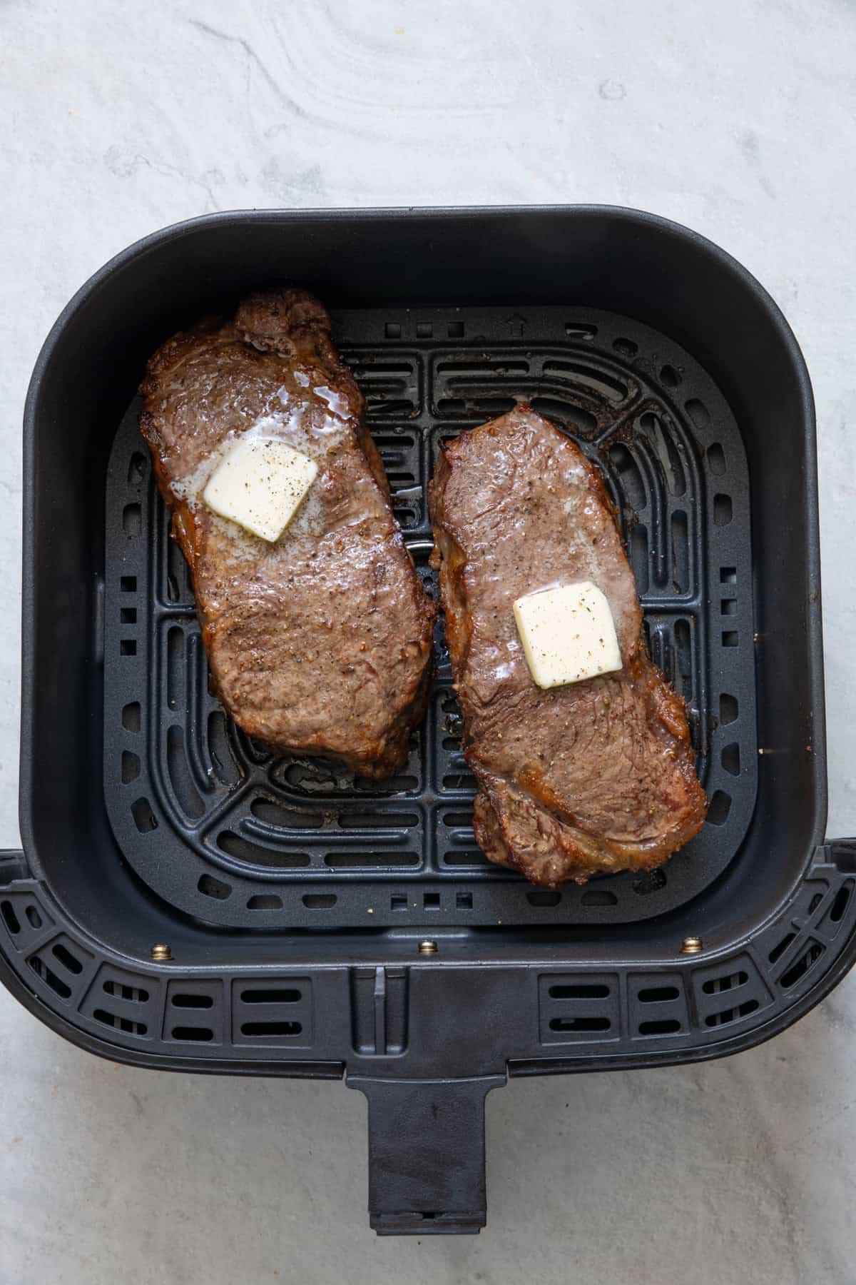 Overhead shot of 2 steaks in air fryer with melted butter, salt, and pepper after being cooked.