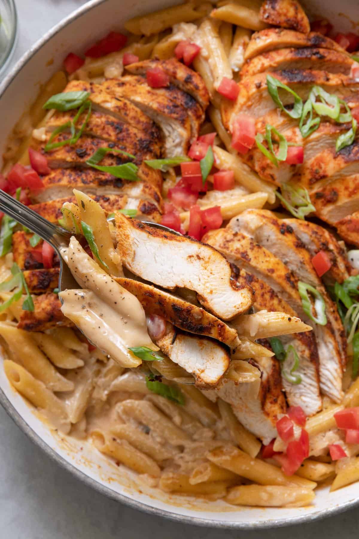 Close up of creamy pasta with chicken with a spoon scooping some of the pasta.