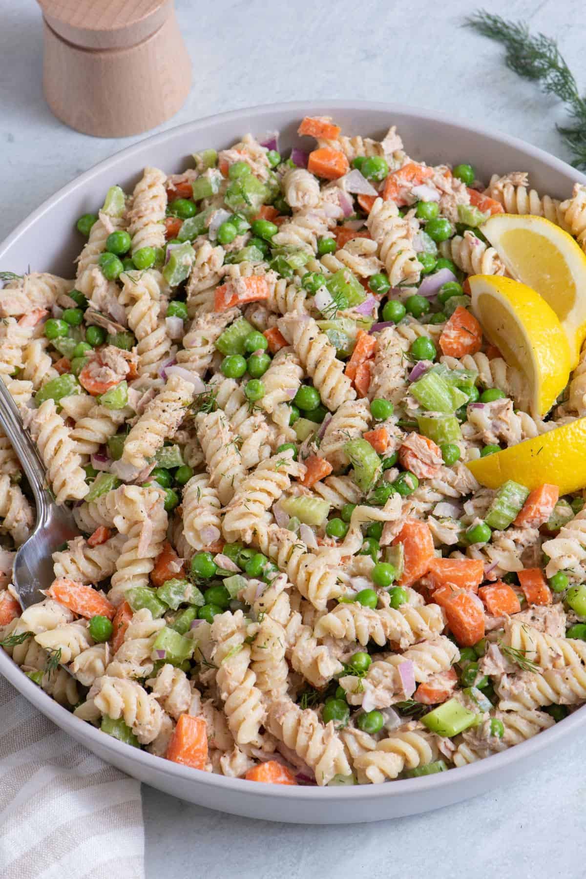 Large bowl of the tuna pasta salad garnished with lemon wedges.