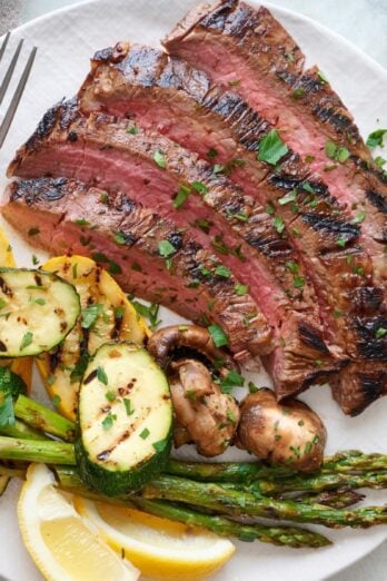Grilled flank steak on a plate with grilled vegetables.