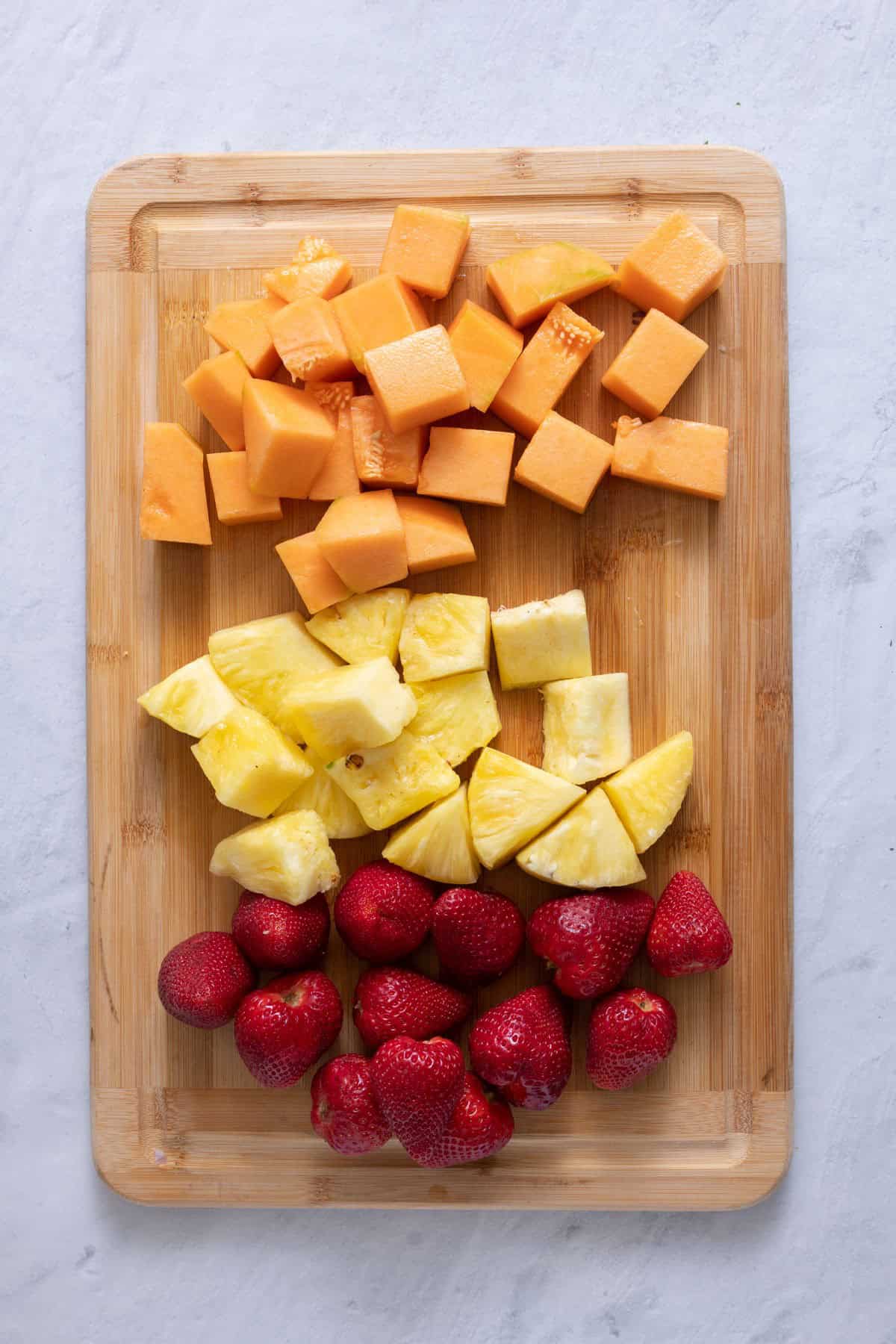 Cut up fruit sectioned on a cutting board.