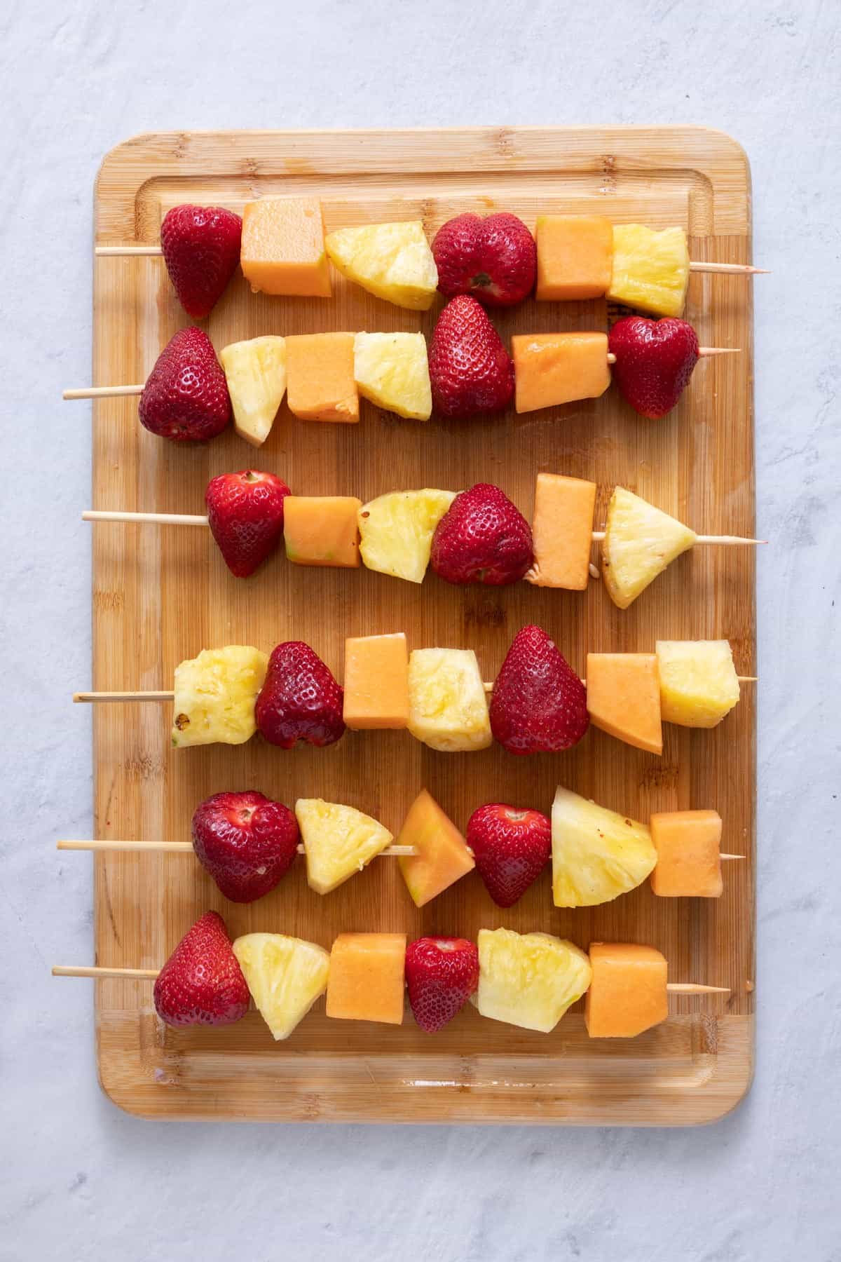 Cut fruit skewered on kabob sticks laid on a cutting board.