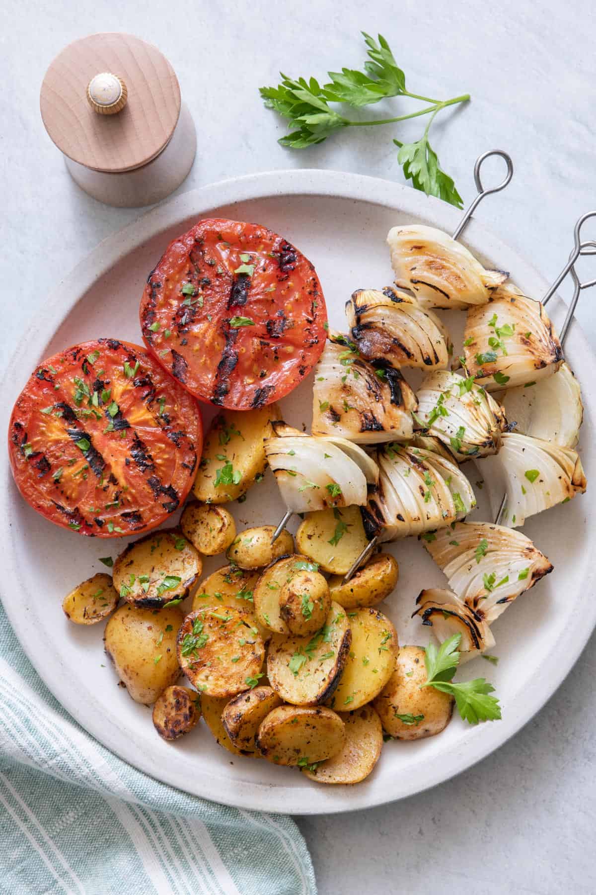Plate with grilled onion chunks on skewers served with grilled tomatoes and grilled potatoes.