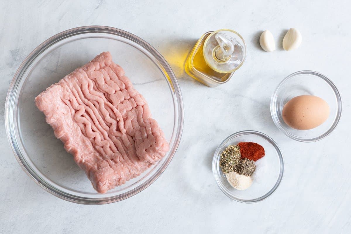 Ingredients for recipe: ground turkey in glass bowl, olive oil, 2 garlic cloves, 1 egg, and spices.