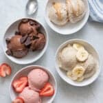 4 Nice cream flavors in white bowls: chocolate with chocolate chunks, strawberry with fresh strawberries on top, vanilla banana with banana slices on top, and peanut butter nice cream with a drizzle of peanut butter on top.