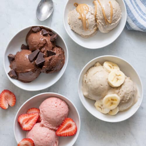 4 Nice cream flavors in white bowls: chocolate with chocolate chunks, strawberry with fresh strawberries on top, vanilla banana with banana slices on top, and peanut butter nice cream with a drizzle of peanut butter on top.
