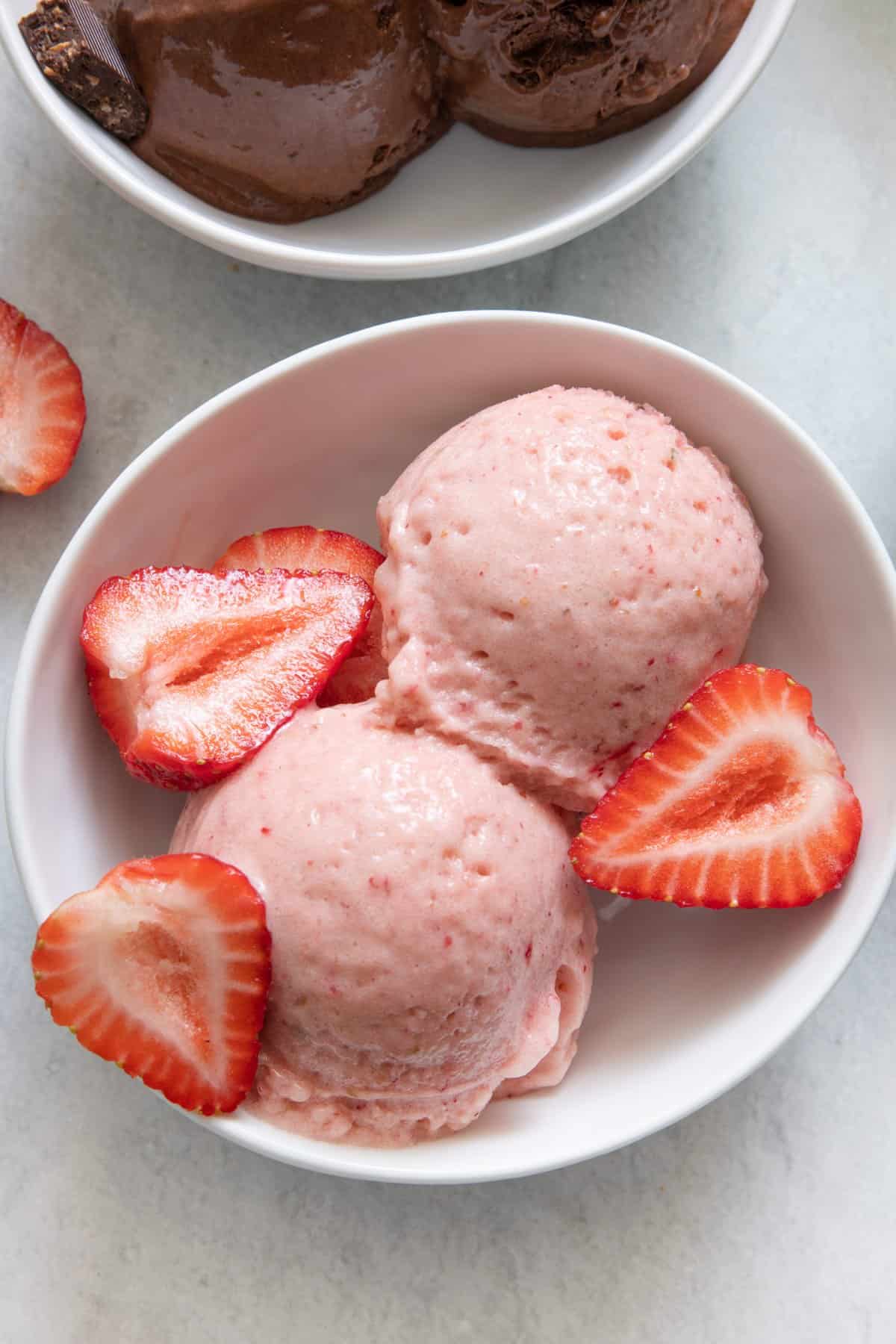 Strawberry Nice Cream in white bowl with pieces of fresh strawberries added and chocolate nice cream off to side.